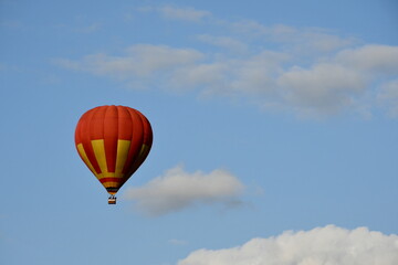 Close up on a red and yellow balloon with a big basket underneath flying through the cloudy sky full of clouds next to a dense forest or moor seen on a sunny summer day on a Polish countryside