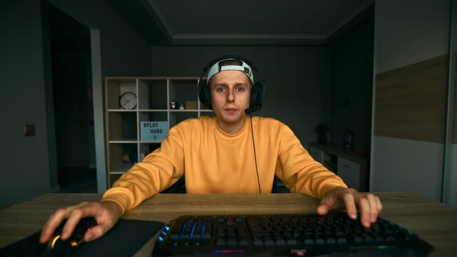 Handsome young man in a headset on his head playing free time online games with friends on the computer and talking into a microphone with a smile on his face. Gaming concept