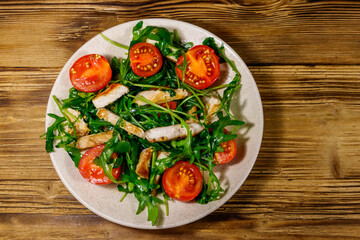 Tasty salad of fried chicken breast, fresh arugula and cherry tomatoes on wooden table. Top view