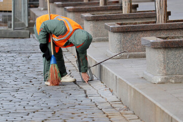 Street cleaning, female municipal worker in uniform sweeping the sidewalk with a broom. Janitor in...