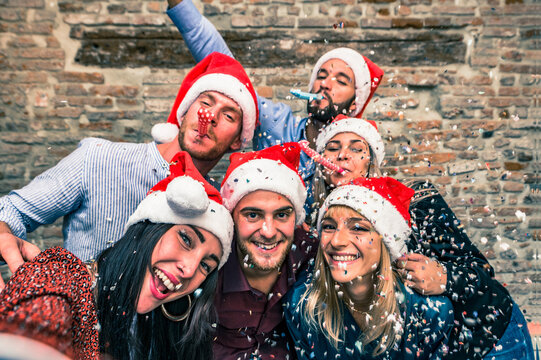 Group of happy friends with the face mask down in Christmas night they throw confetti and blow into the trumpets. - Group of young coworkers.celebrating Christmas wearing  Santa hats - focus center