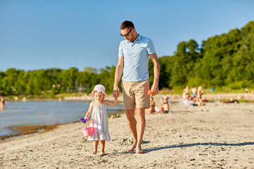 family, fatherhood and leisure concept - happy father walking with little daughter on beach