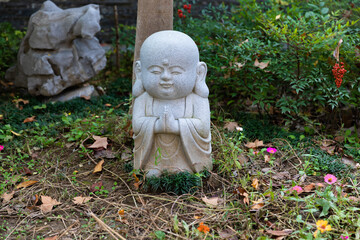 A small statue of a little monk praying at a garden in historic Buddhist Jinshan Temple, Zhenjiang, Jiangsu, China.