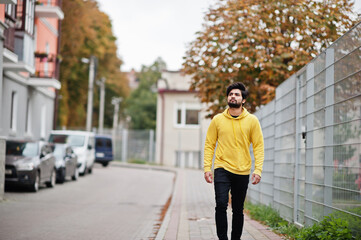 Urban young hipster indian man in a fashionable yellow sweatshirt. Cool south asian guy wear hoodie walking on fall street.