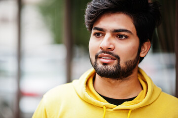 Close up portrait of urban young hipster indian man in a fashionable yellow sweatshirt. Cool south asian guy wear hoodie.