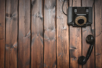 Black rotary phone on the brown wooden desk background with copy space.