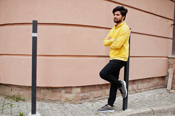 Urban young hipster indian man in a fashionable yellow sweatshirt. Cool south asian guy wear hoodie.