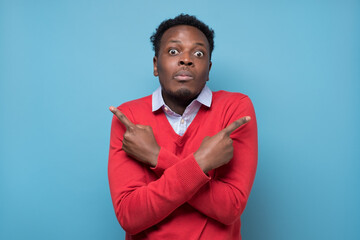 Confused african man pointing in two different directions, not sure which way to go, hesitant to...