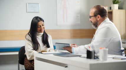 Obraz premium Doctor Consultation Office: Hispanic Female Patient Listens to Experienced Physician who Uses Digital Tablet Computer to Show, Explain Her Analysis Results, Give Advice, Prescribe Medicine.