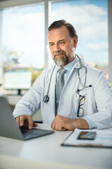 In a Doctor's Consultation Office: Experienced Physician Working on a Laptop, Prescribing Medicine, Analysing Tests Results. Health Care Specialist Planning Treatment. Vertical Portrait Shot.