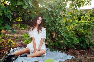 beautiful woman in white dress drinks from a glass of wine at a picnic in the vineyard