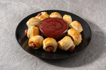 Pigs in blankets. Mini sausages wrapped in puff pastry with ketchup sauce. 