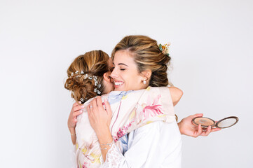 Beautiful blonde woman in white dress on her wedding day before getting married, her mother hugs her.