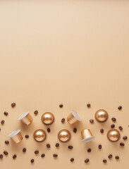 Caffeine, hot drinks and objects concept - close up of golden capsules or pods for coffee mashine with some roasted grains on beige background. Top view with space for text. Flat lay..