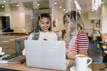 Smiling multiracial females friends communicating and using modern technologies for searching...
