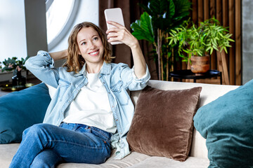 Happy young woman doing selfie by phone at home
