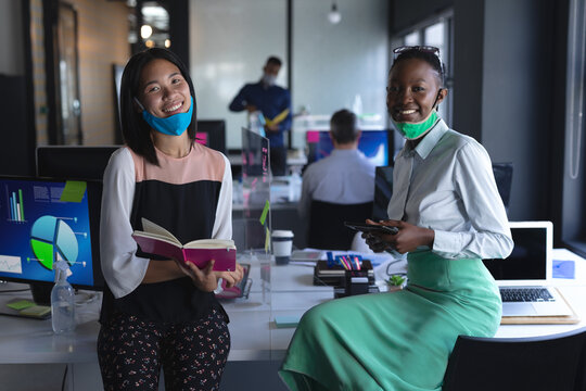 Portrait of asian woman with book and african american woman with digital tablet at modern office