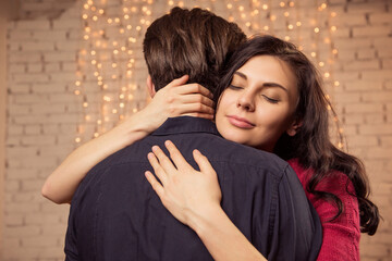 Beautiful brunette caucasian romantic loving couple in cozy warm sweaters in the cabin on a christmas new year eve, smiling, kissing, having fun with each other. Dim dark night light, toned image