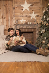 Naklejka premium Beautiful brunette caucasian romantic loving couple in cozy warm sweaters in the cabin on a christmas new year eve, smiling, kissing, having fun with each other. Dim dark night light, toned image