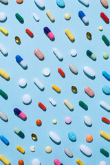 Creative layout of colorful pills and capsules on blue background with summer sun and sharp shadow. Minimal medical concept. Pharmaceutical, Covid-19 or Coronavirus. Flat lay, top view.