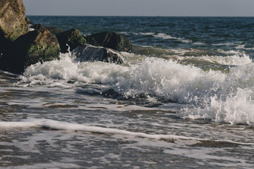 Sea wave spreading on the beach became a sea foam near the rocks