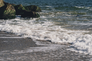 Sea wave spreading on the beach became a sea foam near the rocks