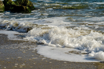 Sea wave spreading on the beach became a sea foam near the rocks