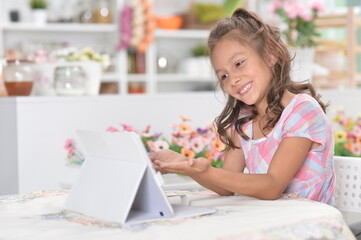 Little girl sitting at table and using modern tablet