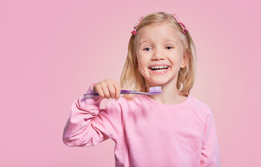 Happy child girl with toothbrush, brushes teeth and smiles on gray background. Free space for advertisement. Oral hygiene.