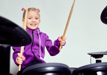 Happy caucasian kid girl drummer. Girl playing on elettronic drum kit or learns to play drums in...