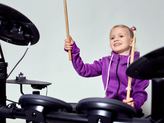 Happy caucasian kid girl drummer. Girl playing on elettronic drum kit or learns to play drums in...