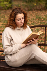 Obraz premium a young beautiful girl is sitting on a bench in an autumn Park, reading a book 