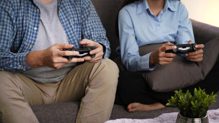 Excited funny young couple playing video games holding game controller sitting on sofa having fun with new technology console online at home at night
