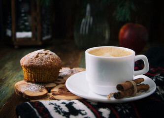 
White cup of coffee and cinnamon sticks on blurred christmas background