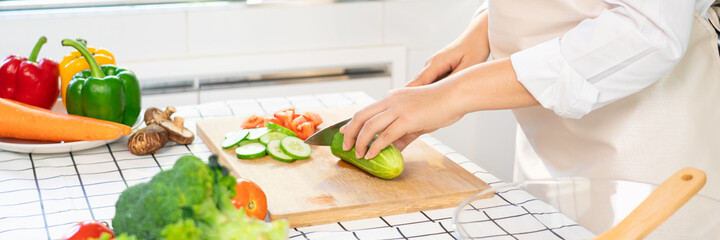 young Asian woman is preparing healthy food vegetable salad by Cutting cucumber for ingredients on cutting board on light kitchen, Cooking At Home and healthy food concept.