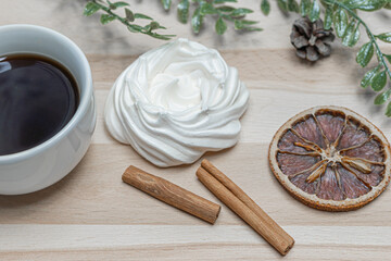 A mug of coffee on a wooden table, airy meringue, dried orange slice, cinnamon and winter holiday accessories. New year christmas card