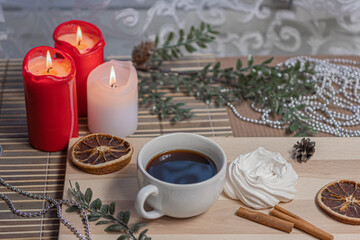 Obraz na płótnie Canvas Christmas candles, a mug of coffee on a wooden table, airy meringue, dried orange slice, cinnamon and winter holiday accessories. New Year