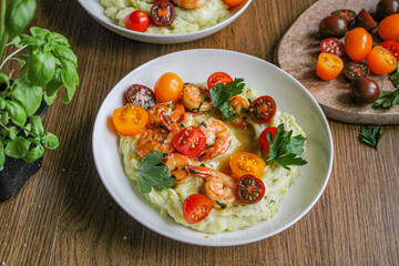 Glazed shrimp with garlic and honey sauce over creamy mashed potatoes and topped with colourful cherry tomatoes and coriander leaves. Beautiful spring meal plated on wooden table. 