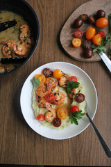 Glazed shrimp with garlic and honey sauce over creamy mashed potatoes and topped with colourful cherry tomatoes and coriander leaves. Beautiful spring meal plated on wooden table. 