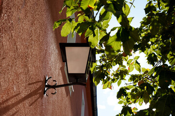 Low angle view of an outdoor lamp on an orange all next to trees on a sunny day