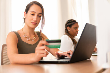 Brazilian business woman using credit card and laptop for payment in coworking office. E-commerce, online shopping, communication concept..
