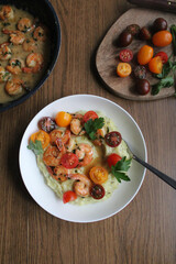 Glazed shrimp with garlic and honey sauce over creamy mashed potatoes and topped with colourful cherry tomatoes and coriander leaves. Beautiful spring meal plated on wooden table. 