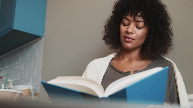 Pleased african woman indoors at home reading a book