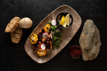 Hot appetizer with chicken fillet, grilled corn and vegetables. Unusual hot dish with bread on a dark background.