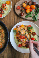 Glazed shrimp with garlic and honey sauce over creamy mashed potatoes and topped with colourful cherry tomatoes and coriander leaves. Beautiful spring meal plated on wooden table. 