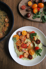 Glazed shrimp with garlic and honey sauce over creamy mashed potatoes and topped with colourful cherry tomatoes and coriander leaves. Beautiful spring meal plated on wooden table. 