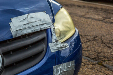 A deformed bonnet of a blue car is provisionally repaired with an adhesive tape