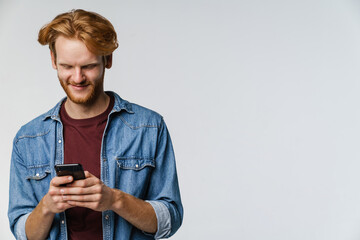 Fototapeta premium Joyful caucasian redhead guy smiling while using cellphone
