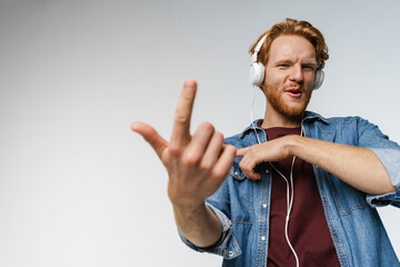 Naklejka premium Happy redhead guy in headphones showing finger at camera and dancing