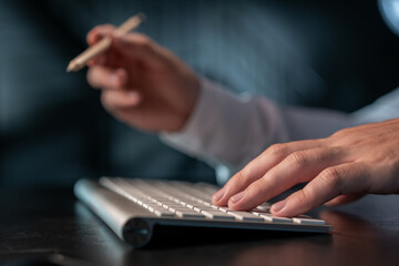 Office manager male hands typing on computer keyboard, closeup. Businessman working, holding a pencil in right hand, typing on the wireless keyboard with the left, concept of office work